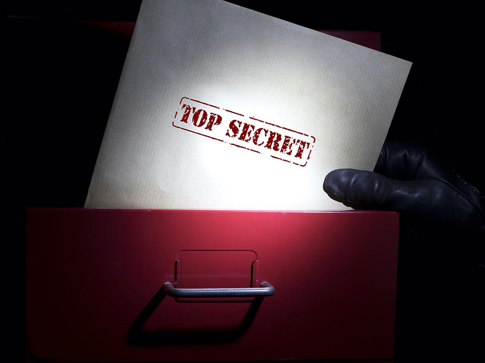 A gloved hand holds a file stamped 'Top Secret' in red letters. It is being taken from a red filing cabinet.