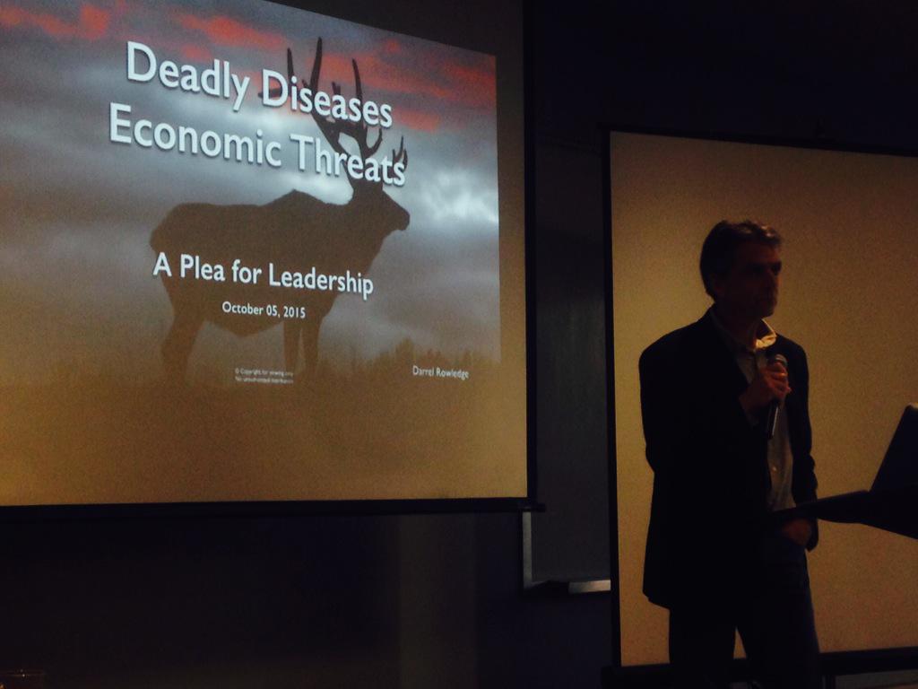 In a darkened room, a man gives a presentation in front of a screen that says ‘Deadly Diseases. Economic Threats.’