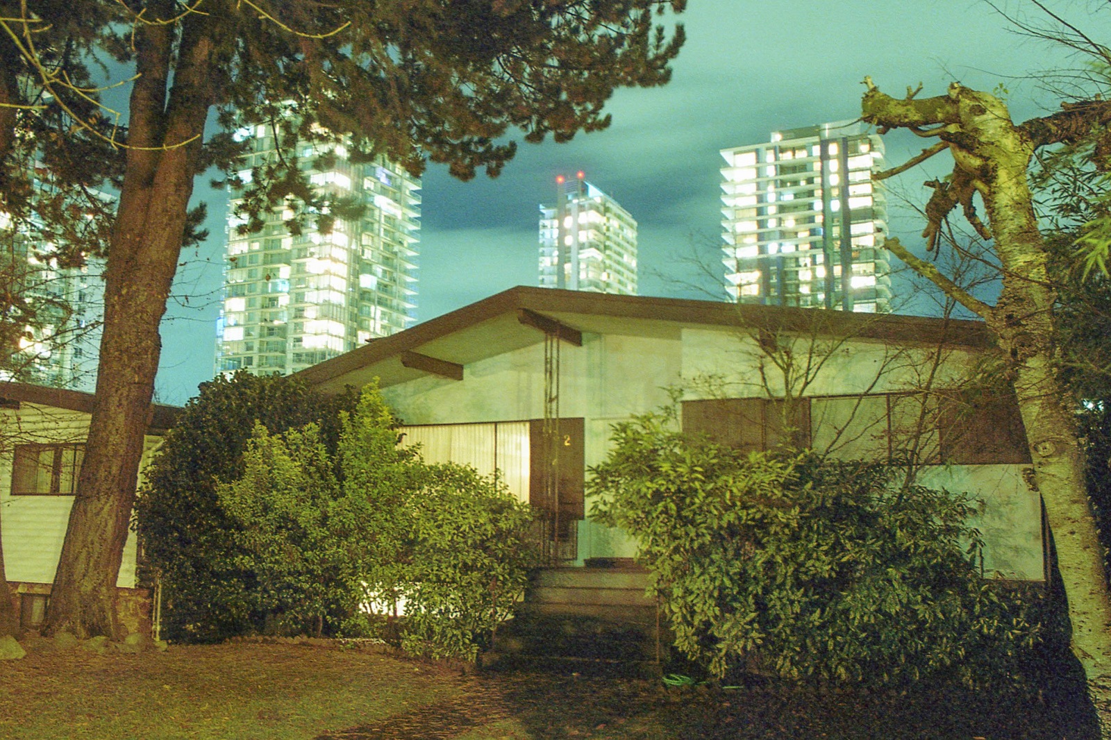 A house with lights on at night with bright towers looming behind.