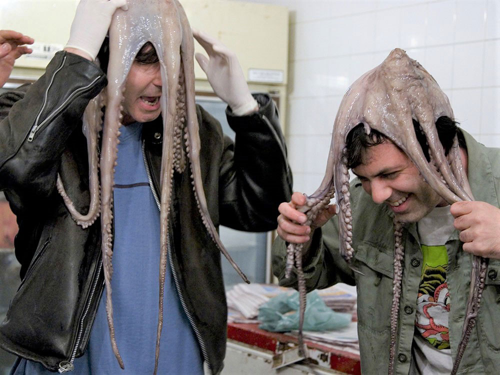 Spencer Rice, left, is wearing white latex gloves, a black leather jacket over a blue T-shirt and a live octopus over his head. Kenny Hotz, right, is in a green shirt with another octopus over his head. Hotz is smiling while Rice looks shocked.