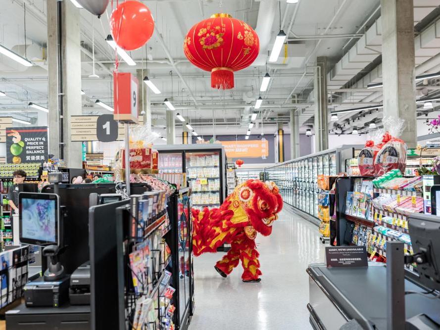 A bright-red lion dancer shows up in the aisles of a brightly lit supermarket.