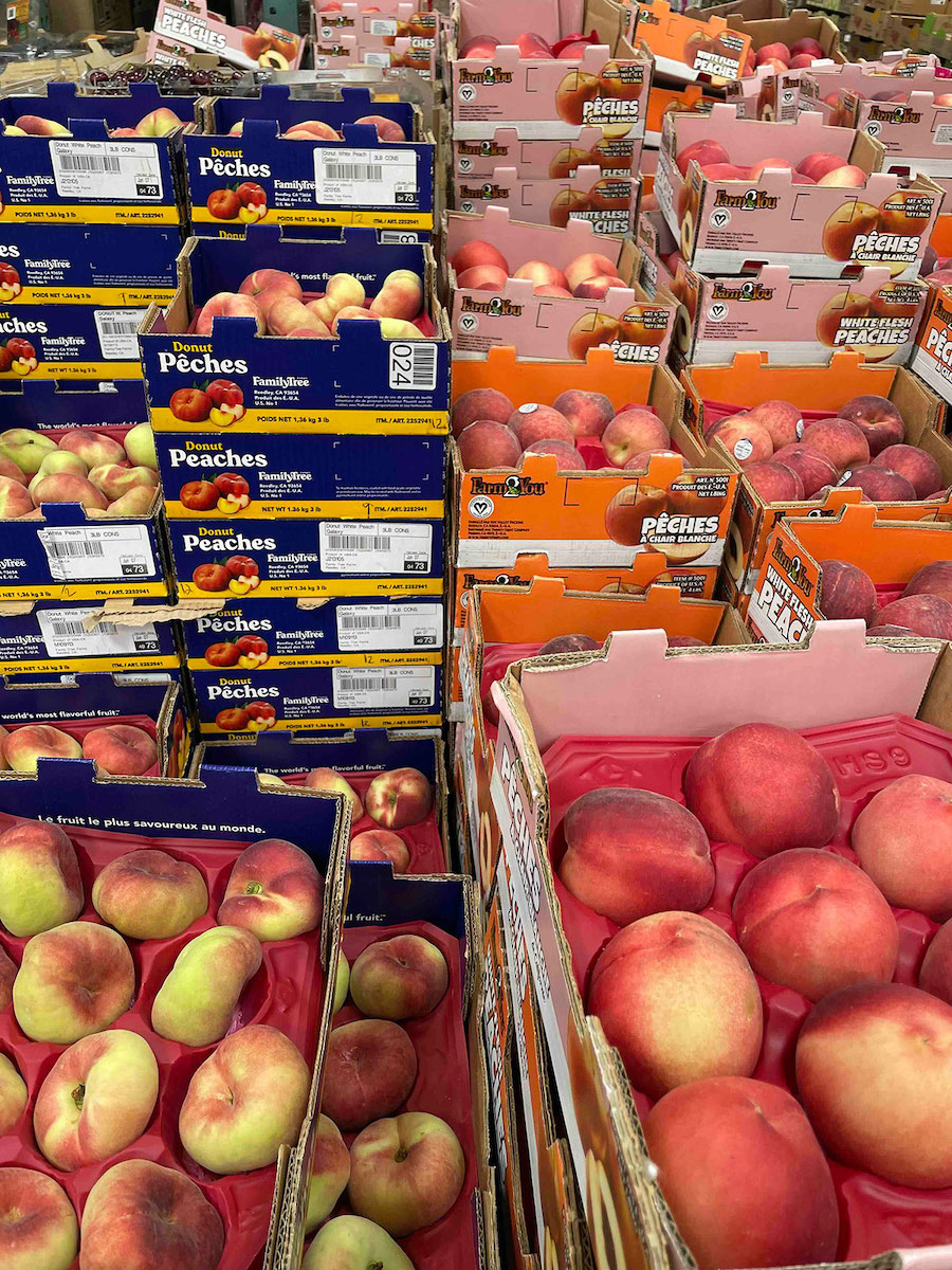 Colourful cardboard flats of peaches with blue and pink packaging stand in tight, stall stacks in a supermarket.