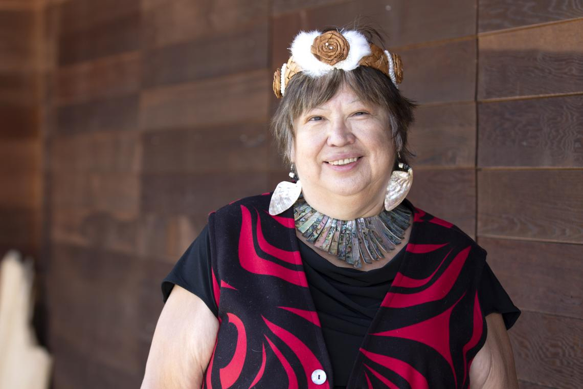 BC First Nations Justice Council director Judith Sayers, a light-skinned woman with dark hair, wears a traditional headband, oyster shell earrings and an oyster shell necklace. She smiles slightly, looking directly at the camera.