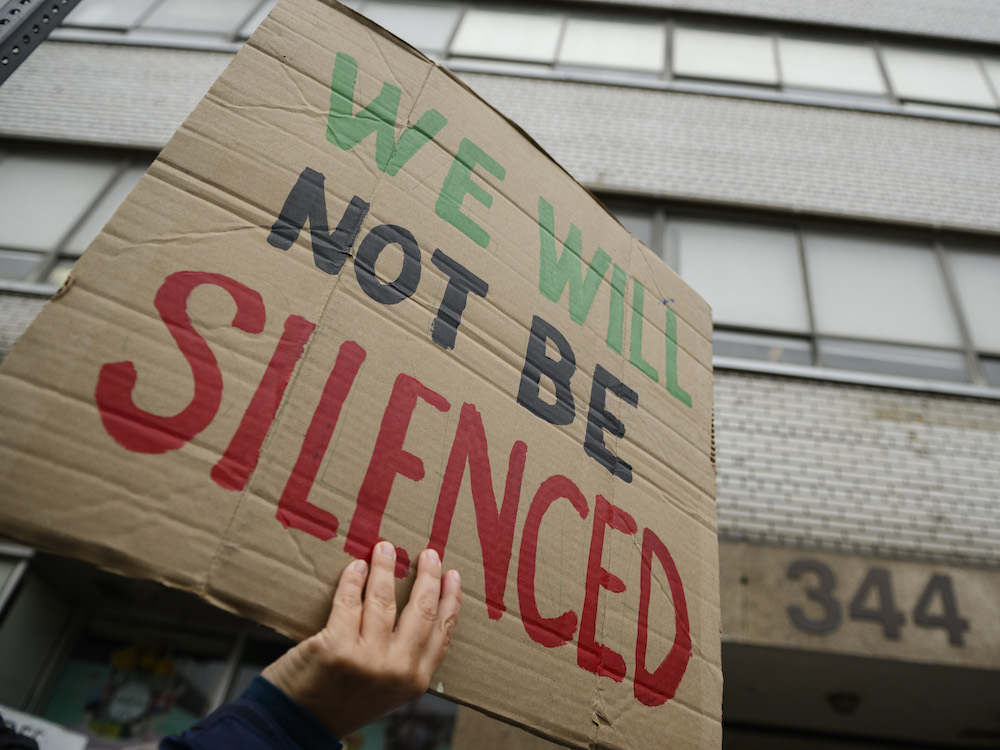 A protester holds a sign reading "We Will Not Be Silenced."