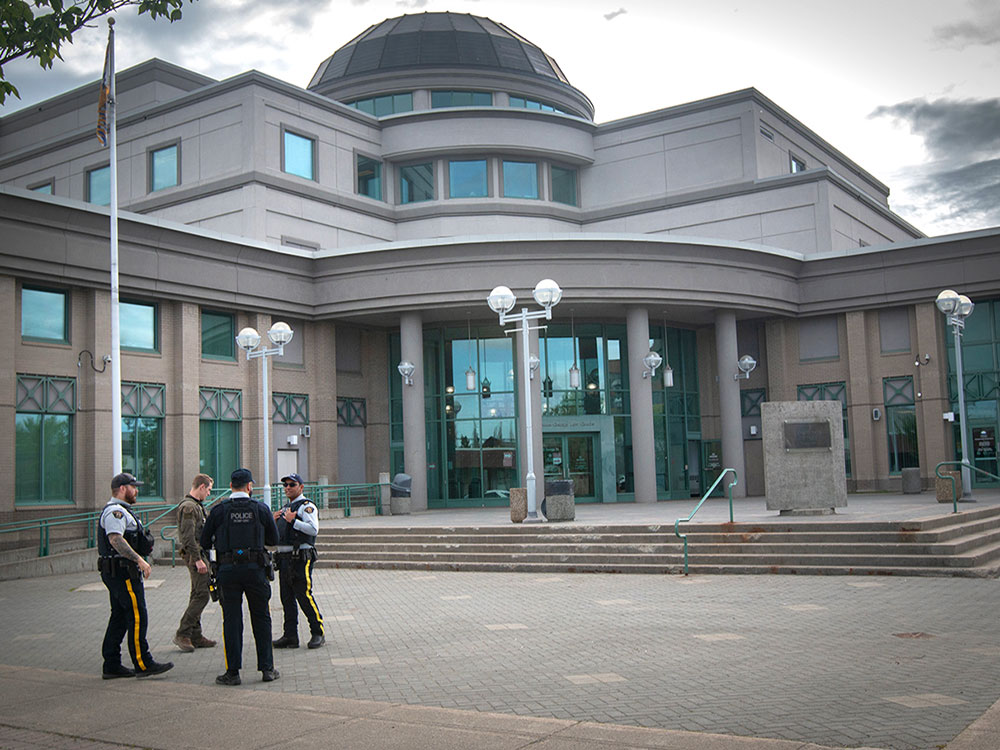 Four uniformed police officers stand in a circle in front of a large, concrete building.