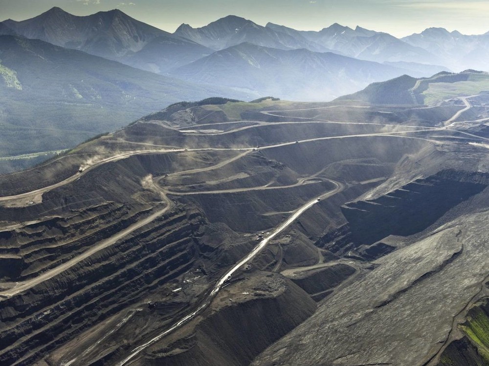 Looking down into a giant coal mine carved out of a mountaintop. Terraces and roads lead to a deep pit; mountains loom in the background.