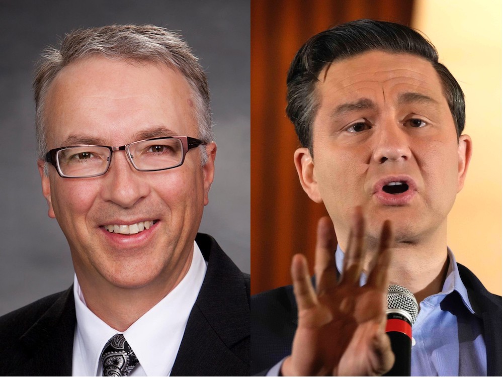 On the left, a middle-aged white man with short hair and glasses, wearing a black jacket, white shirt and patterned tie. On the right, a middle-aged white man with black hair, a dark jacket and blue shirt with no tie.